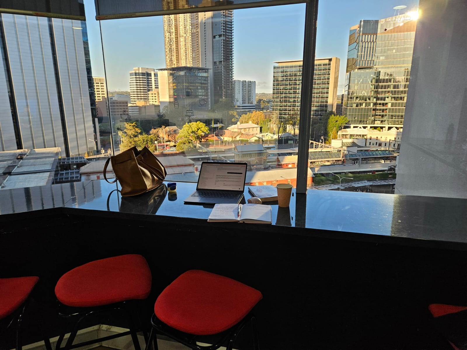Afternoon sunlight over Parramatta, with Rodah’s open notebook and laptop at the window