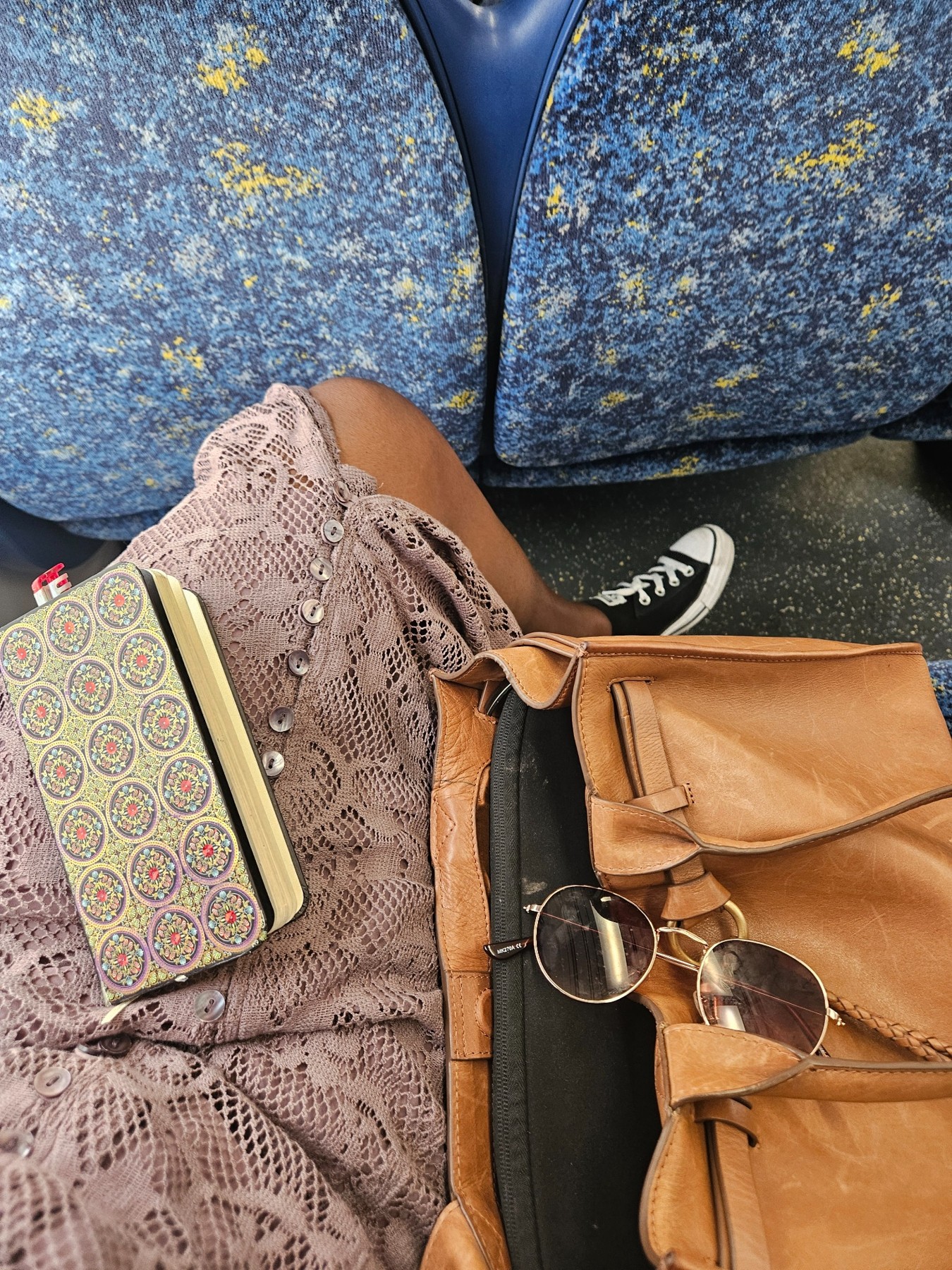 My notebook and brown bag beside me on a blue patterned seat